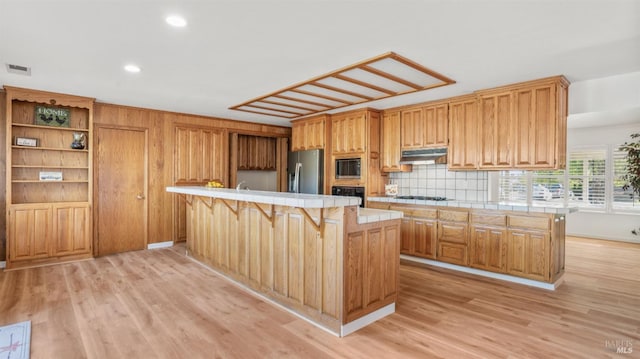 kitchen featuring a kitchen breakfast bar, light hardwood / wood-style flooring, tile counters, a kitchen island, and stainless steel appliances