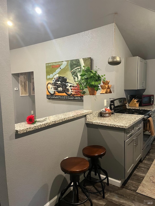 kitchen featuring gray cabinetry, stainless steel gas stove, dark hardwood / wood-style floors, and a breakfast bar