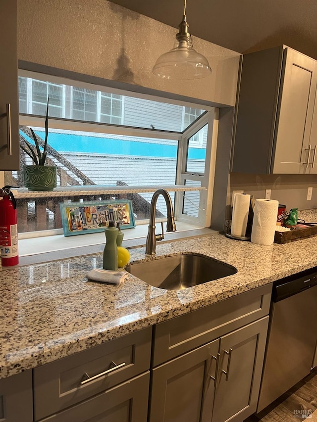 kitchen with light stone countertops, dishwasher, sink, pendant lighting, and gray cabinets