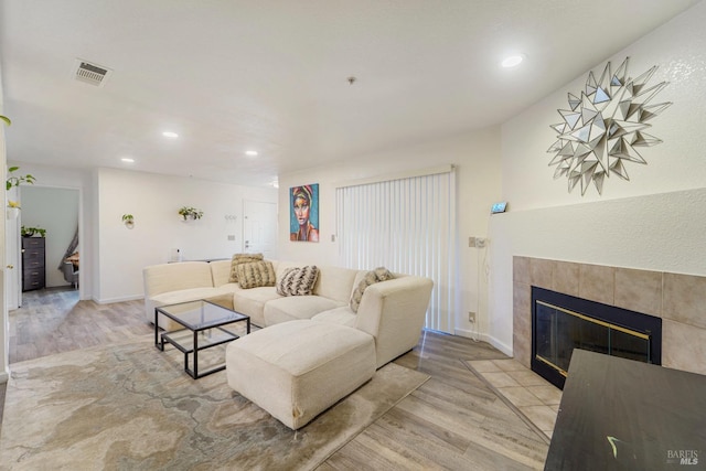 living room featuring light wood-type flooring, visible vents, a tiled fireplace, and recessed lighting