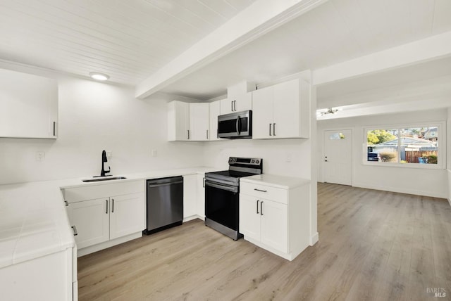 kitchen with appliances with stainless steel finishes, beamed ceiling, white cabinetry, sink, and light wood-type flooring