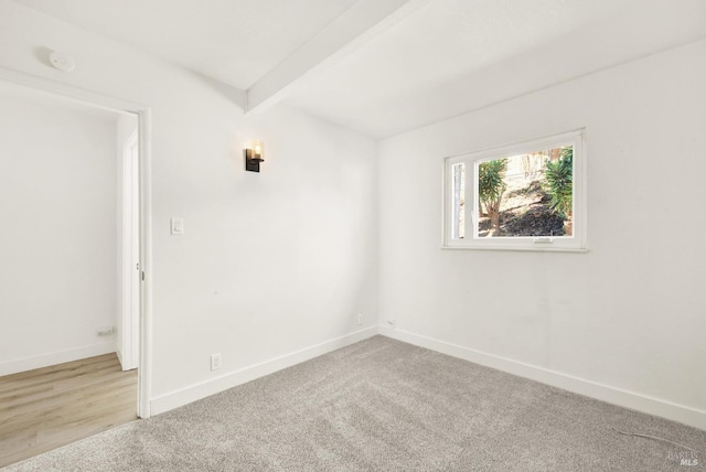 spare room featuring beamed ceiling and light colored carpet