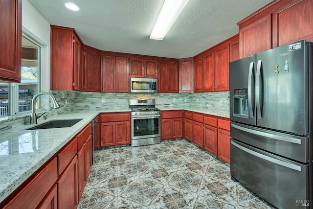 kitchen featuring decorative backsplash, appliances with stainless steel finishes, light stone counters, and sink