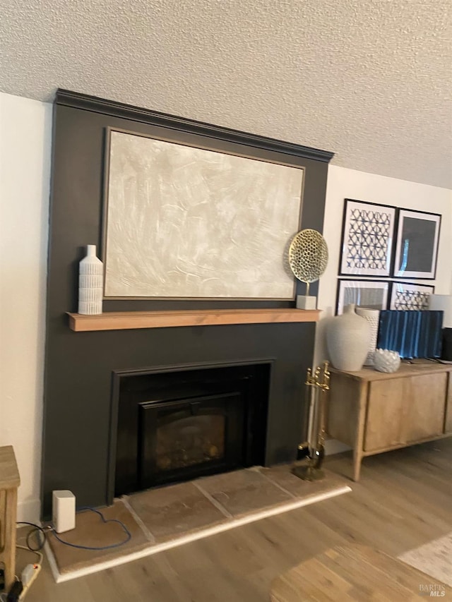 details with a textured ceiling, wood finished floors, and a glass covered fireplace