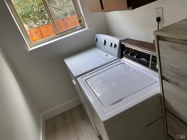 laundry room featuring washer and clothes dryer, cabinet space, and light wood-style flooring