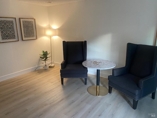 sitting room with light wood-style floors, baseboards, and a textured ceiling