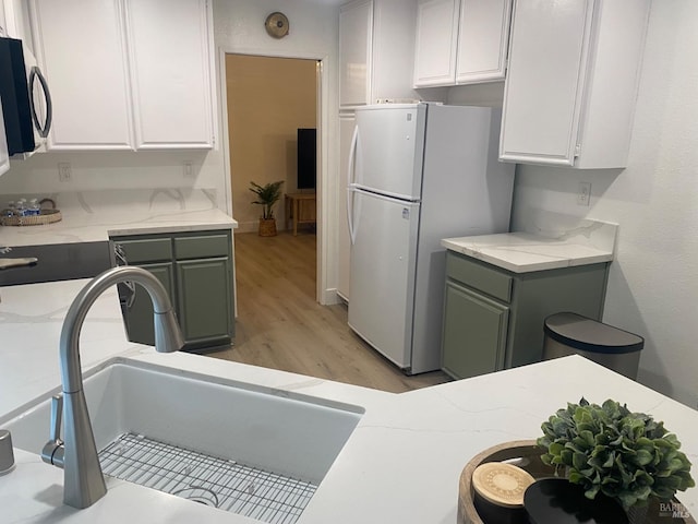 kitchen with light wood-style flooring, stainless steel microwave, freestanding refrigerator, white cabinetry, and a sink