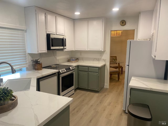 kitchen featuring light stone counters, appliances with stainless steel finishes, light wood-style floors, white cabinetry, and a sink