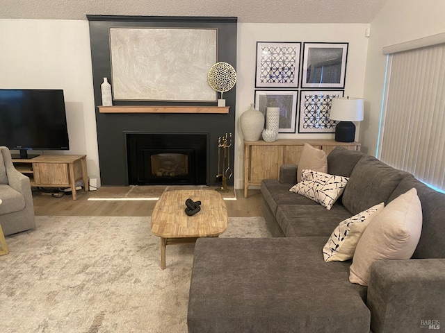 living room featuring lofted ceiling, a fireplace with raised hearth, a textured ceiling, and wood finished floors