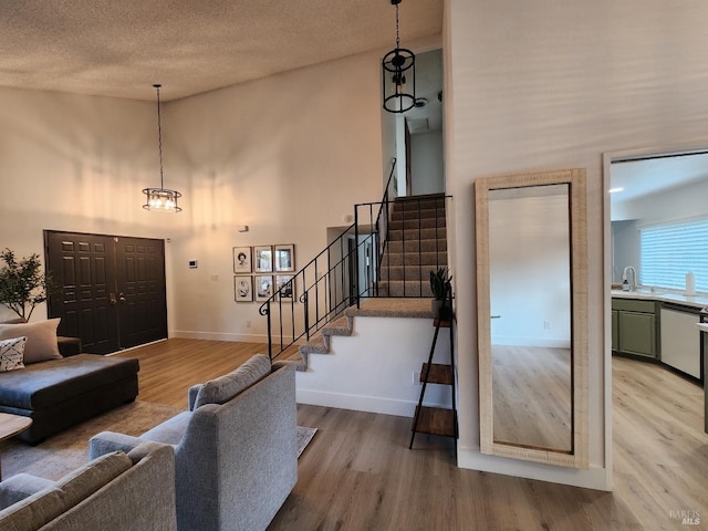 living area featuring a towering ceiling, a textured ceiling, light wood-type flooring, baseboards, and stairs