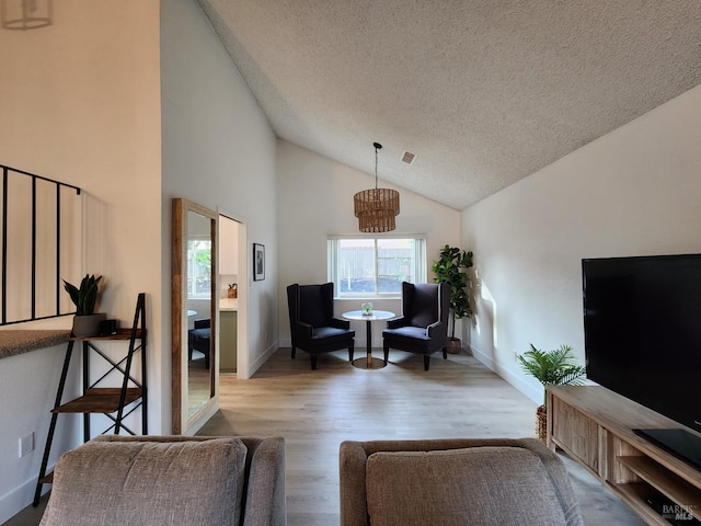 living area with baseboards, visible vents, a textured ceiling, and light wood finished floors