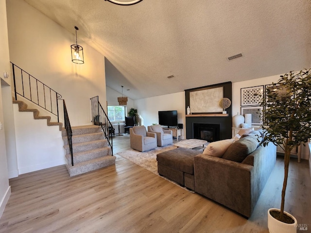 living area with a fireplace, visible vents, a textured ceiling, wood finished floors, and stairs