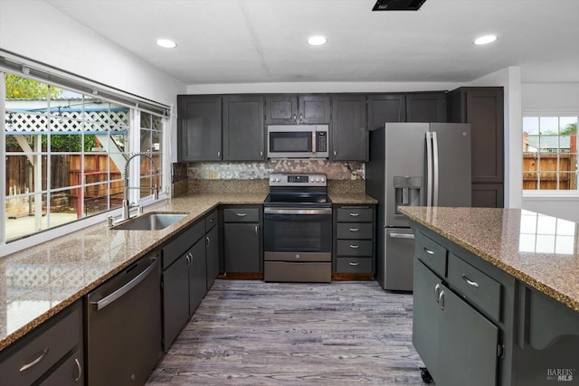 kitchen with sink, light hardwood / wood-style flooring, appliances with stainless steel finishes, tasteful backsplash, and light stone counters