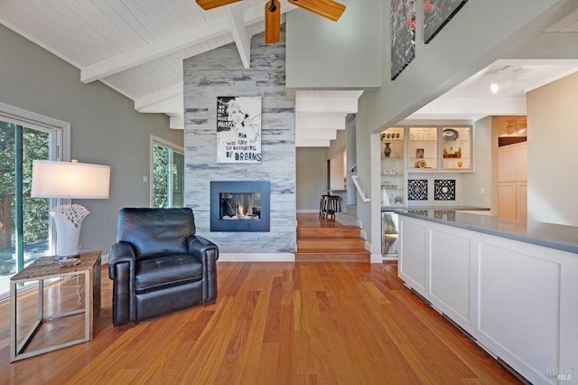 living room with a tile fireplace, ceiling fan, light hardwood / wood-style flooring, beamed ceiling, and high vaulted ceiling