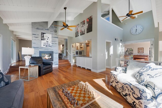 living room with a tile fireplace, high vaulted ceiling, ceiling fan, beamed ceiling, and wood-type flooring