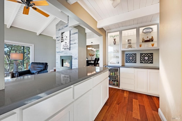 kitchen with dark wood-type flooring, white cabinets, ceiling fan with notable chandelier, lofted ceiling with beams, and beverage cooler