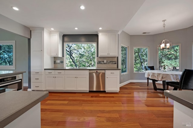 kitchen with light wood-type flooring, tasteful backsplash, stainless steel appliances, a notable chandelier, and white cabinets