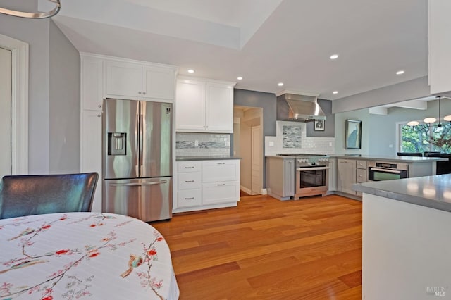 kitchen with light wood-type flooring, backsplash, wall chimney exhaust hood, stainless steel appliances, and white cabinetry