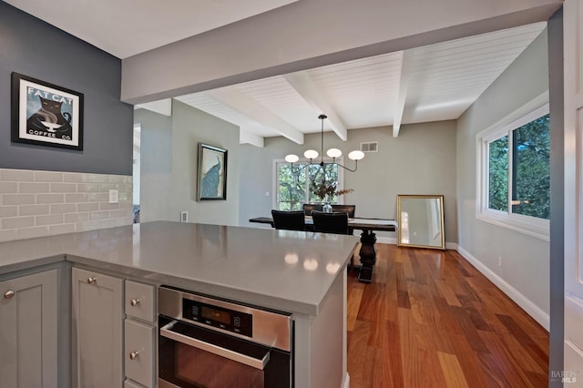 kitchen with beamed ceiling, kitchen peninsula, decorative light fixtures, and oven