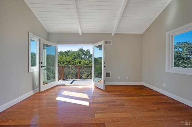 unfurnished room featuring vaulted ceiling with beams, a healthy amount of sunlight, and wood-type flooring