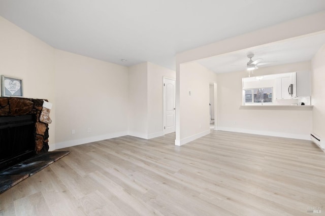 living room with ceiling fan, light wood-type flooring, and a stone fireplace