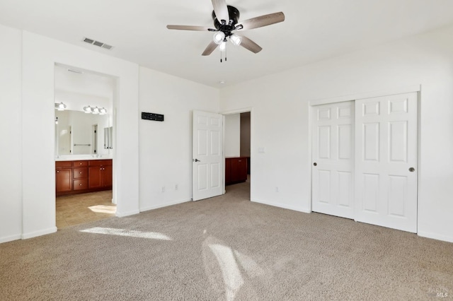 unfurnished bedroom featuring light carpet, connected bathroom, a closet, and ceiling fan