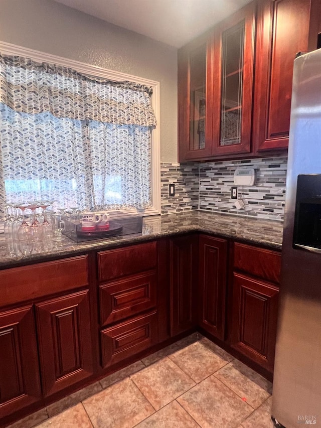 kitchen featuring tasteful backsplash, stainless steel refrigerator with ice dispenser, dark stone countertops, and light tile patterned floors