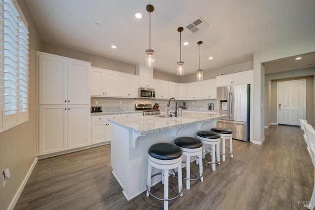 kitchen with white cabinets, appliances with stainless steel finishes, sink, hanging light fixtures, and a kitchen island with sink