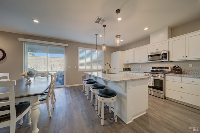 kitchen featuring decorative light fixtures, a center island with sink, sink, white cabinetry, and stainless steel appliances