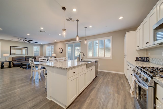 kitchen with white cabinetry, stainless steel appliances, a kitchen island with sink, decorative light fixtures, and light stone counters