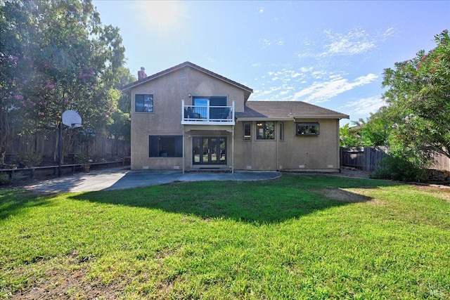 rear view of house with a lawn, a balcony, a patio, and french doors