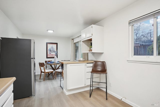 kitchen featuring kitchen peninsula, a breakfast bar, light hardwood / wood-style flooring, white cabinetry, and stainless steel refrigerator