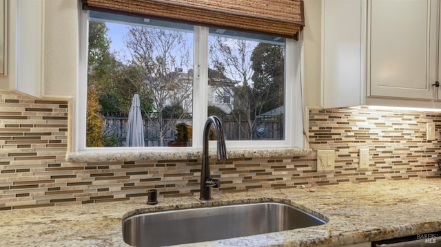 room details with tasteful backsplash, sink, light stone countertops, and white cabinets