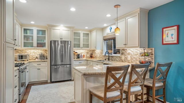 kitchen featuring a sink, appliances with stainless steel finishes, a kitchen bar, glass insert cabinets, and pendant lighting