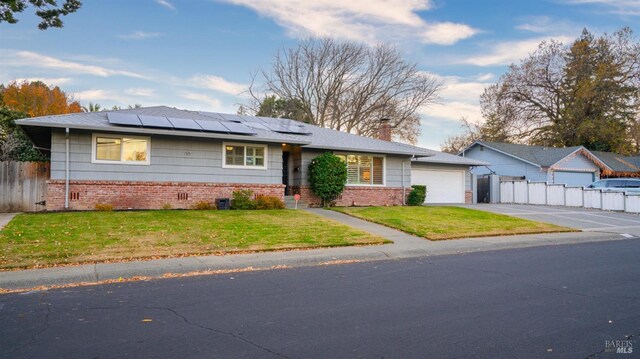 ranch-style home featuring a garage, a front yard, and solar panels