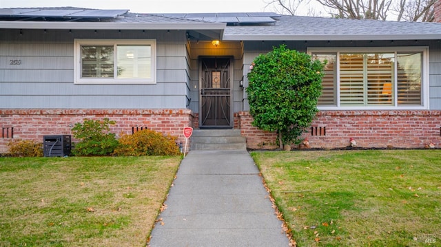 entrance to property featuring crawl space, brick siding, a lawn, and a shingled roof