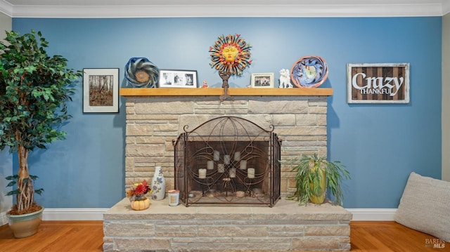 room details with crown molding, a stone fireplace, baseboards, and wood finished floors