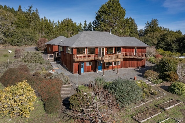 back of property featuring a vegetable garden, driveway, and a wooden deck