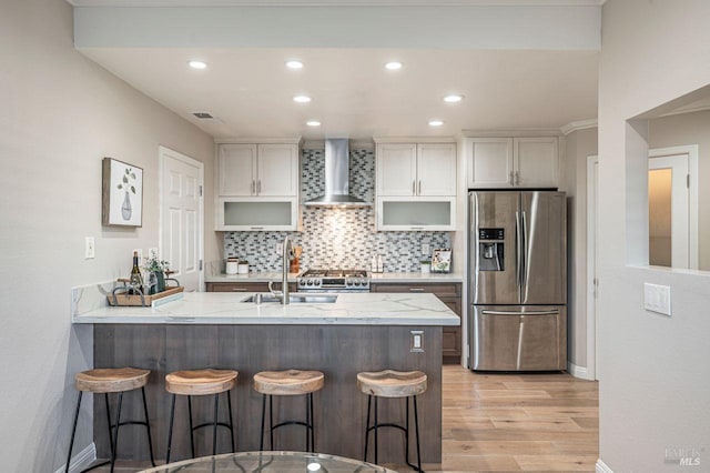 kitchen with wall chimney exhaust hood, stainless steel appliances, light hardwood / wood-style floors, a kitchen bar, and sink