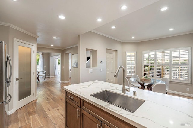 kitchen with sink, light stone countertops, light hardwood / wood-style floors, and stainless steel fridge