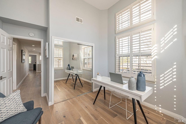 home office with light hardwood / wood-style flooring and a towering ceiling