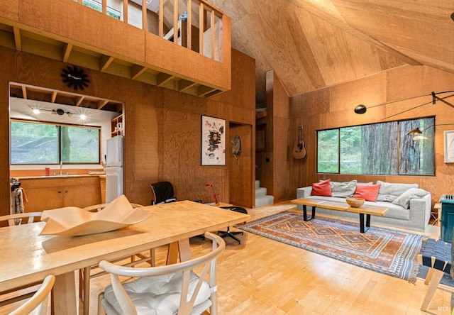 living room featuring wood-type flooring, high vaulted ceiling, wooden walls, and sink