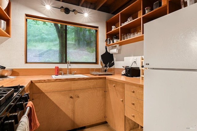 kitchen with butcher block countertops, stainless steel gas stove, sink, and white refrigerator