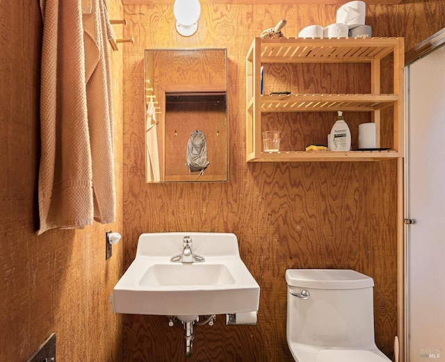 bathroom with wood walls, toilet, and sink