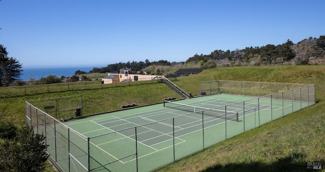 view of tennis court featuring a water view and a lawn