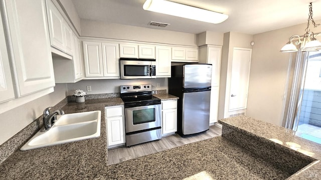 kitchen featuring appliances with stainless steel finishes, sink, white cabinets, a chandelier, and light hardwood / wood-style flooring