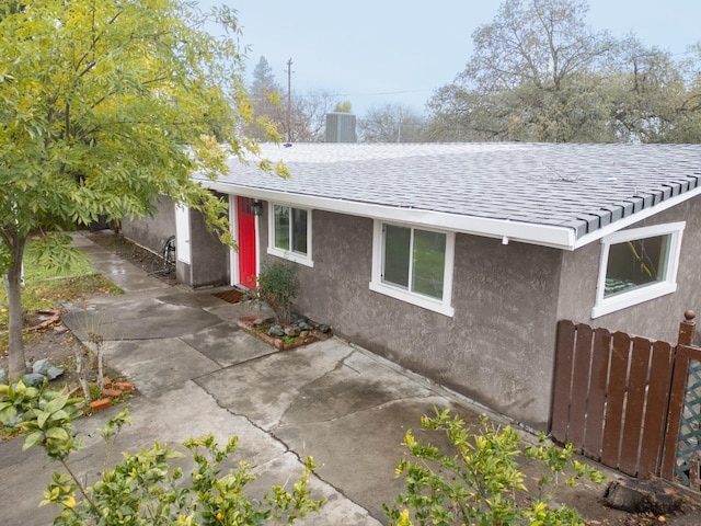 view of front facade featuring central air condition unit, stucco siding, fence, and roof with shingles