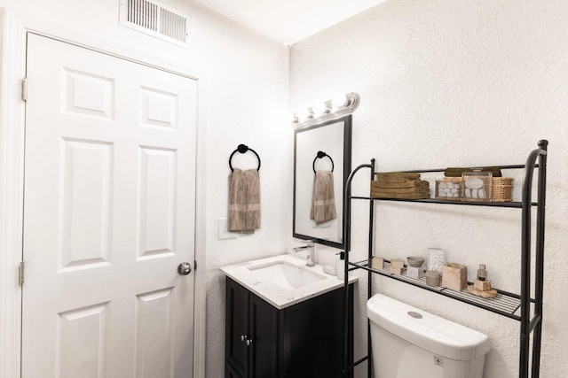 bathroom with toilet, a textured wall, vanity, and visible vents