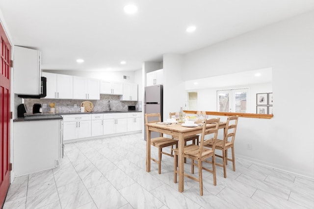 kitchen featuring vaulted ceiling, stainless steel refrigerator, sink, white cabinetry, and backsplash