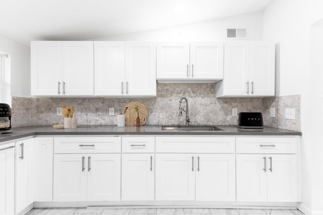 kitchen featuring lofted ceiling, a sink, visible vents, decorative backsplash, and dark countertops